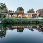Gesamtansicht des Hauses von der Seeseite mit Spiegelung im Wasser und beleuchtetem Wohnbereich.