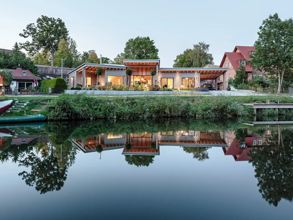 Gesamtansicht des Hauses von der Seeseite mit Spiegelung im Wasser und beleuchtetem Wohnbereich.