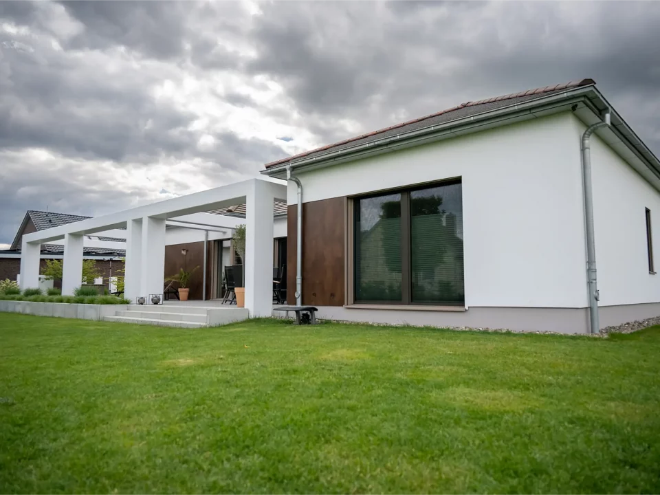 Gesamtansicht der Rückseite des Einfamilienhauses mit gepflegtem Garten, schlichter weißer Fassade und modernen Fensterflächen.