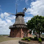 Historische Windmühle mit Backsteinbau und hölzernem Rundbalkon, eingebettet in die weite Landschaft – denkmalgerechte Instandsetzung durch MALER GROSSER.